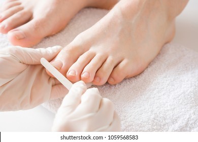Pedicurist's hands in protective rubber gloves filing toenails with nail file. Cares about man's feet. Specialist with client in beauty salon. Professional beauty service. Pedicure, manicure concept.