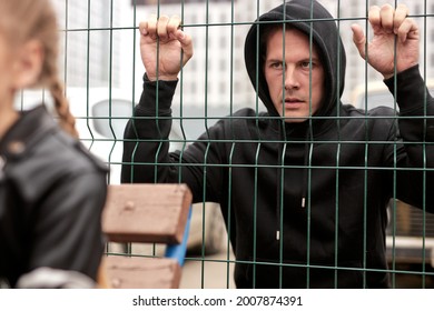 Pedophile watching at child sitting on playground alone, while walking. Kid in danger. Children safety protection kidnapping. Adult caucasian dangerous man in black wear look at kid through fence