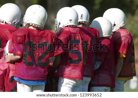 Pee Wee football players in a huddle with red uniforms and white helmets