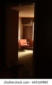 Peeking Into An Abandoned And Neglected Motel Room. A Chair Is In The Distance. Sides Of The Image Are Very Dark. Natural Light.                            