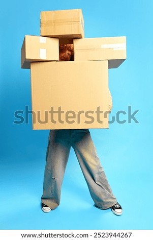 Peeking out from behind stack of cardboard boxes, this person, shopaholic, smiling against blue studio background. Concept of Black Friday sale. Concept of Black Friday, fashion, Flash Sale. Ad
