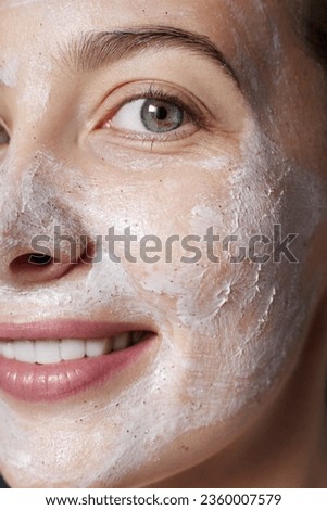 Peel. Skin care facial scrub. Beauty portrait of young happy woman with a white peeling cosmetic product to whole her face. Daily skincare routine. Dermatology. Exfoliating