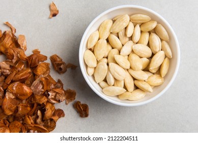 peeled almonds in a white bowl and a peel from it next to a concrete background. concept for a recipe for making almond flour. top view