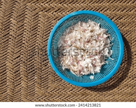 Peeled dry husk of garlic is placed in a plastic basket. Garlic skin. Dry husk of white garlic. Food waste and peelings. Top view. Above view. Photo taken in day sunlight. Close-up photo