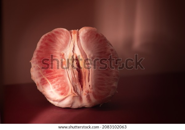 Peeled grapefruit divided in half on a red table,\
dark lighting, feminine health concept. Fruit as a symbol of the\
vagina. without people