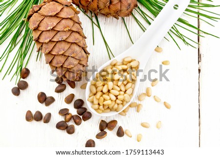 Peeled kernels of cedar nuts in a spoon, two pinecones and nuts in the shell against a light wooden board on top