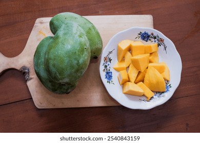 Peeled mango slices on a white plate on wooden cutting board in wooden table background, a whole ripe mango placed beside, Fresh fruit. Tropical fruit - Powered by Shutterstock