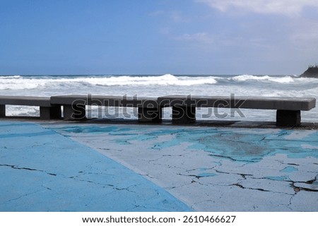 Peeled off weathered blue floor. Empty concrete benches on the coast of Atlantic ocean. Big waves in the winter. Blue sky with white clouds. Moya, Gran Canaria, Canary Islands, Spain.