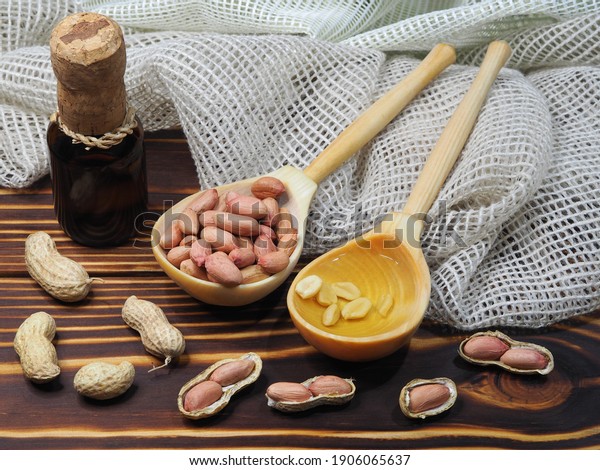 Peeled peanuts, in\
shell nuts, peanut oil in a bottle and a wooden spoon  on a  wooden\
background, closeup, top view. Natural ground nuts arachis hypogaea\
for a healthy diet