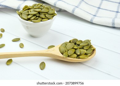 Peeled raw pumpkin seeds on a wooden spoon and in small ceramic bowl. Selective focus on the spoon. Healthy vegan foods, eating plant seeds.