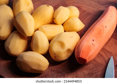 Peeled sweet potatoes and regular potatoes on a wooden cutting board in the kitchen. - Shutterstock ID 2144494853