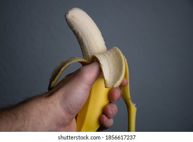 A peeled yellow banana in a human hand is being eaten