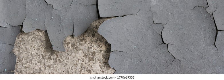 Peeling paint on the wall. Panorama of a concrete wall with old cracked flaking paint. Weathered rough painted surface with patterns of cracks and peeling. Panoramic texture for background and design.