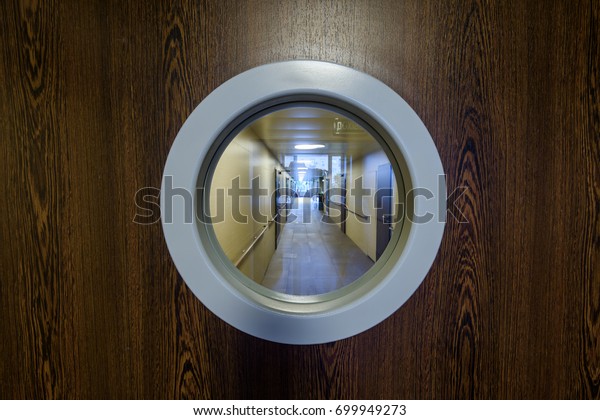 Peephole door, entrance to\
hospital corridor with big eye close-up. Modern wooden door and\
round window, spyhole overlooking hallway in clinic or residential\
building.