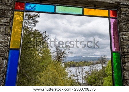 Peering through the stained glass indow frame at Claife viewing station in the Lake District admiring the boats on Lake Windermere.