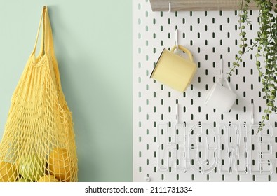 Peg Board With Cups And String Bag Hanging On Green Wall