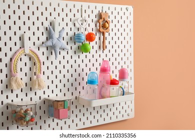 Peg Board With Toys And Bottles Hanging On Beige Wall, Closeup