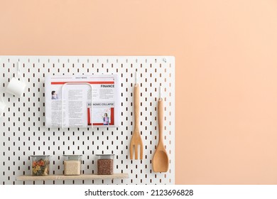 Pegboard With Kitchen Utensils, Newspaper And Jars On Color Wall