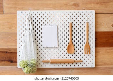 Pegboard With Kitchen Utensils, String Bag With Apples And Notebook On Wooden Wall