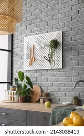 Pegboard With Kitchenware On Grey Brick Wall In Modern Kitchen