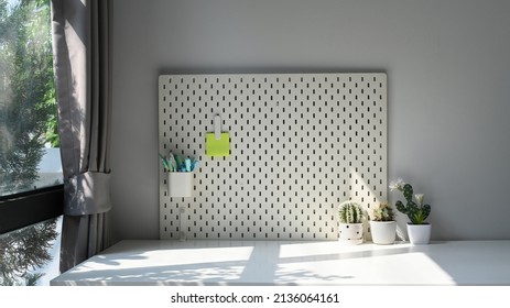 Pegboard With Pencil Holder And Sticky Note Hanging On Light Wall In Home Office.