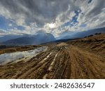 Peja, Kosovo - March 14 2021: A muddy path in the hills near Peja, with a dramatic view of the Accursed Mountains and Rugova Valley under a cloudy sky, showcasing the rugged natural beauty.