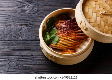 Peking Duck in bamboo steamer with fresh cilantro on black burned wooden background