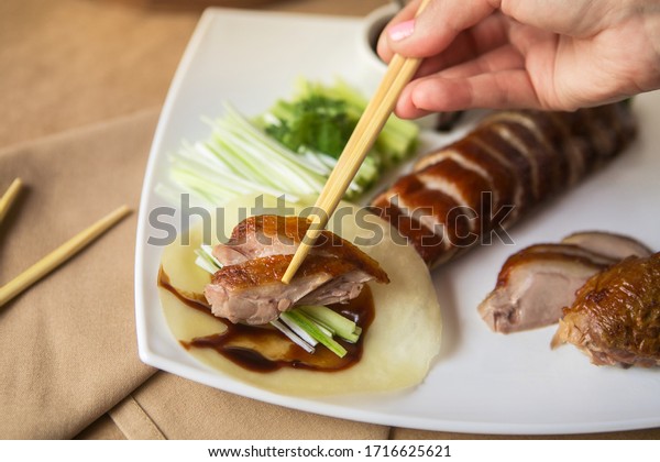 Peking duck cut\
into slices, hands holding sticks with pieces of duck, celery and\
special sauce. Chinese\
cuisine