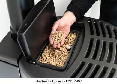 Pellet stove, man holding granules in his hand above a modern black stove - Shutterstock ID 2173484407
