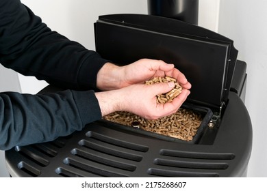 Pellet stove, man holding granules in his hand above a modern black stove - Shutterstock ID 2175268607