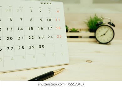 pen, calendar placed on wooden table has retro clock and green plants are background. this image for business, object, decorated, work table concept