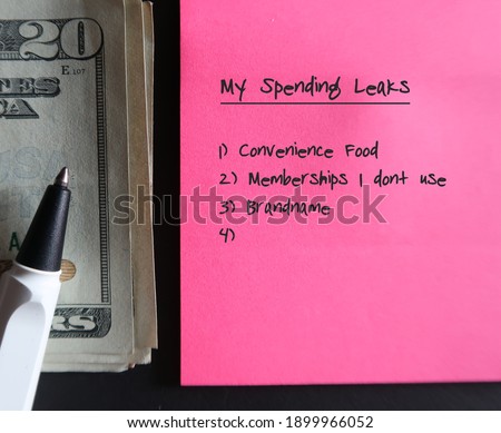Pen, cash money, pencil, pink note with text written MY SPENDING LEAKS and lists of leaks, concept of find out spending weak points to fix them and boost saving