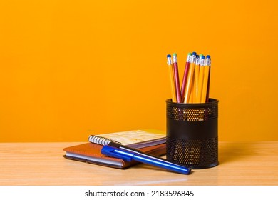 Pen holder metal cup or pot with diary and paper cutter, wooden table and yellow background, back to school concept