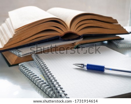 The pen lies on a blank sheet of notebook. Nearby open books and notebooks. Study, scientific work, abstract, study of literature. Background with books, notebooks and pen.