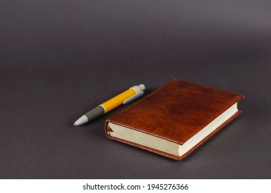 Pen and notebook on a gray background. A yellow and white pen and a closed brown notebook. Selective focus.