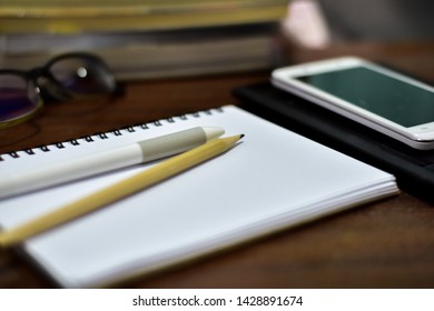 Pen on open diary book ,smart phone,tablet  and glasses on working table.