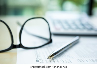 Pen On Tax Form With Blur Calculator And Eyeglasses Background