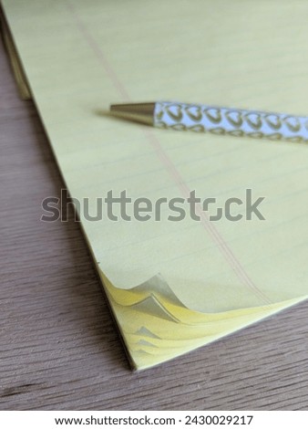 Pen Resting on Yellow College Ruled Paper with Curled Corners 