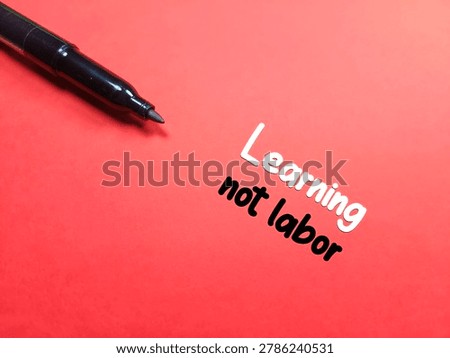 A pen with text Learning not labor on red background. 