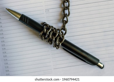 A pen wrapped in an iron chain lies on an empty notebook. Concept- restriction of freedom of speech. - Shutterstock ID 1960794421
