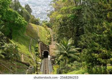 Penang Hill funicular railway in Malaysia, moving down hillside, surrounded by dense tropical forest. Offers panoramic views of lush greenery and city skyline in distance. must-visit spot for tourists - Powered by Shutterstock