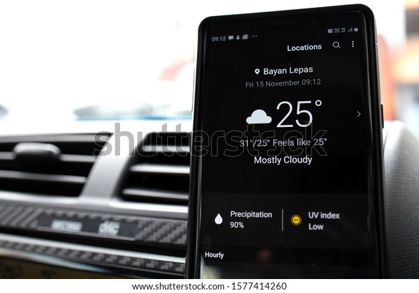 PENANG, MALAYSIA - 15 NOV 2019: User browsing Google\
weather application on Android phone inside the car. Google Weather\
is a most popular weather  forecast service provided by Google inc.\
 