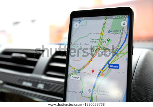 PENANG, MALAYSIA -\
15 NOV 2019: Driver using a Google Maps App on mobile phone in the\
car. Google Maps is a most popular web mapping service for mobile\
provided by Google inc. \
