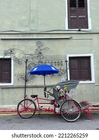 Penang, Malaysia - 5 April 2022: Old Red Trishaw, Three Wheels Vintage Stop Beside Street In George Town, Penang Town Area. Soft Focus