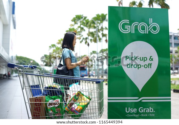 PENANG, MALAYSIA - AUGUST 27, 2018 : Passenger is\
waiting for Grab car at pick up location. Grab is a Singapore based\
company that offers ride-hailing and logistics services through its\
app.