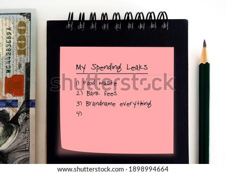 Pencil, cash dollars money, notebook , pink note with text written MY SPENDING LEAKS and lists of leaks, concept of find out spending weak points to fix them and boost saving