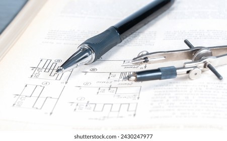 The pencil and circlet are on an open page of a technical reference book with electrical diagrams close up. - Powered by Shutterstock