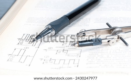 The pencil and circlet are on an open page of a technical reference book with electrical diagrams close up.