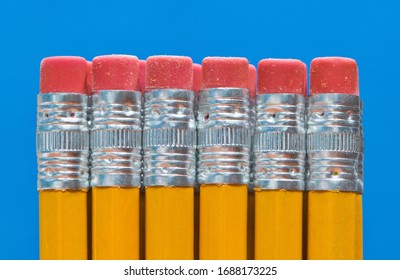 Pencil ends with eraser tips lined up in a straight line in front of a blue background. Macro abstract close up.