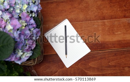 Pencil and notebook on a wooden table near the blue hydrangeas.